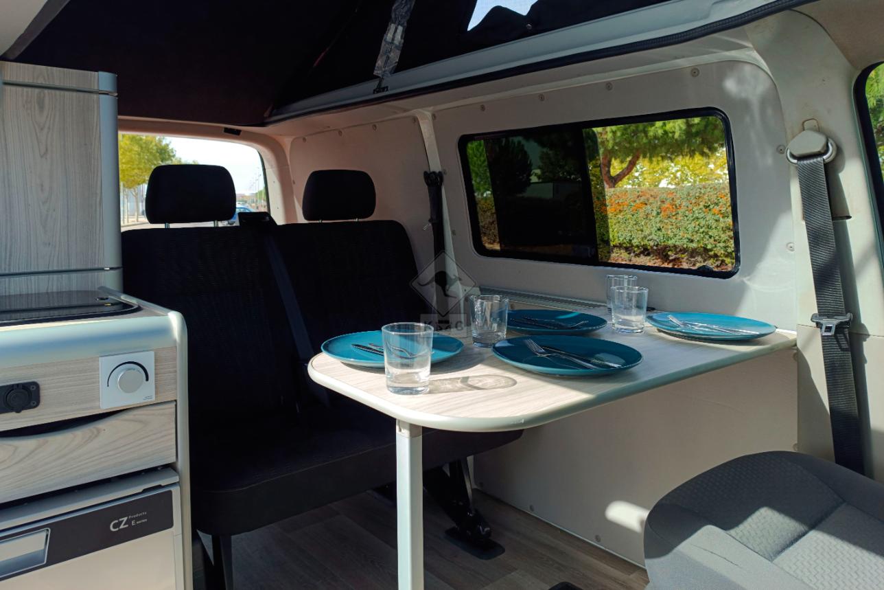 Mesa interior de la camper en alquiler extendida y con vasos y platos