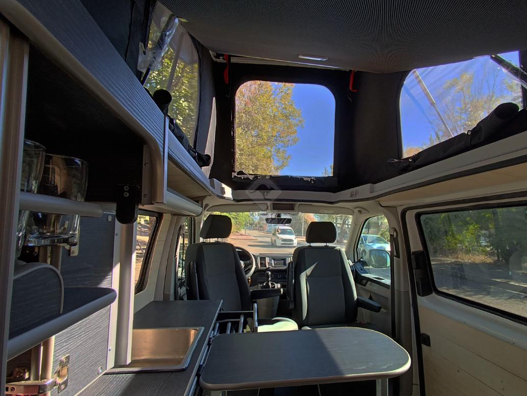 Vista interior de la camper con mesa extendida desde parte trasera