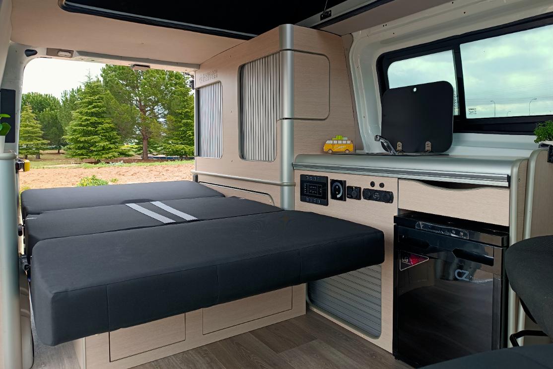 Camper Ford Melbourne en alquiler con la mesa puesta vista de la cama extendida