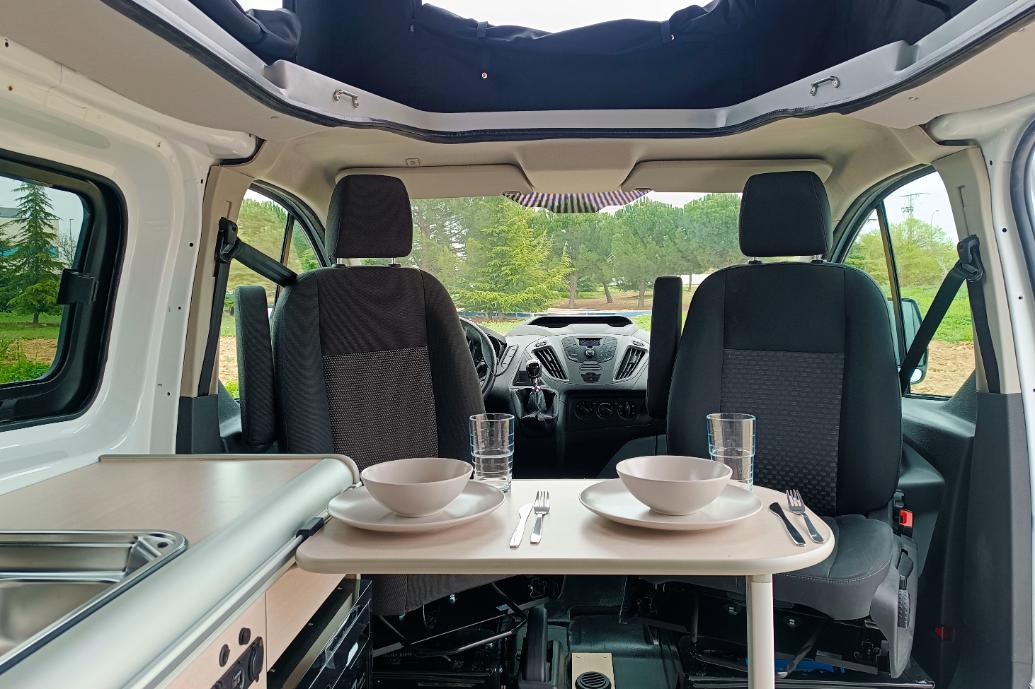 Camper Ford Melbourne en alquiler con la mesa puesta vista a los asientos delanteros